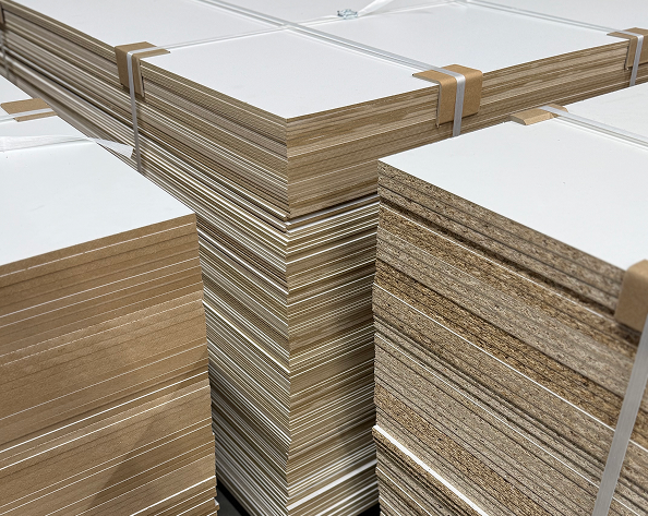 Mehrere weiße Holzplatten sind in einem Regal gestapelt. Der Fokus liegt auf den Kanten der Platten, unscharfer Hintergrund.